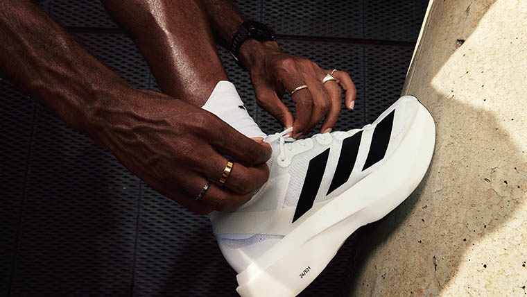 A man doing up the shoe laces of a black and white Adizero Adios Pro Evo 1 (Photo)