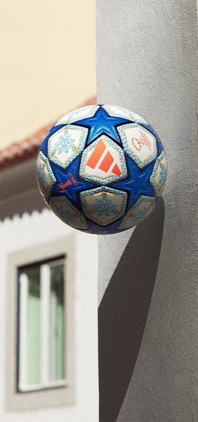 The image shows a large soccer ball resting against a wall, with part of a building in the background. 