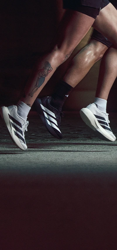 The image is an action photo showing a person running or training indoors. There are shoes against a black background. The shoes appear to be athletic footwear, possibly a model for advertisement given their placement in relation to the person's foot.
