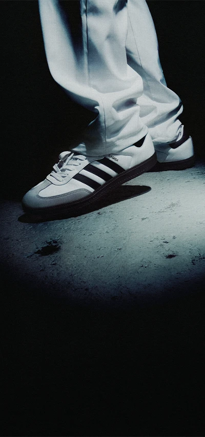 The photo shows a person's leg and foot, dressed in adidas active wear and adidas training shoes, both in black color with white stripes.