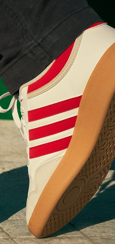 The image shows a person wearing a red and white Adidas sneaker with an orange and gray sole. 
