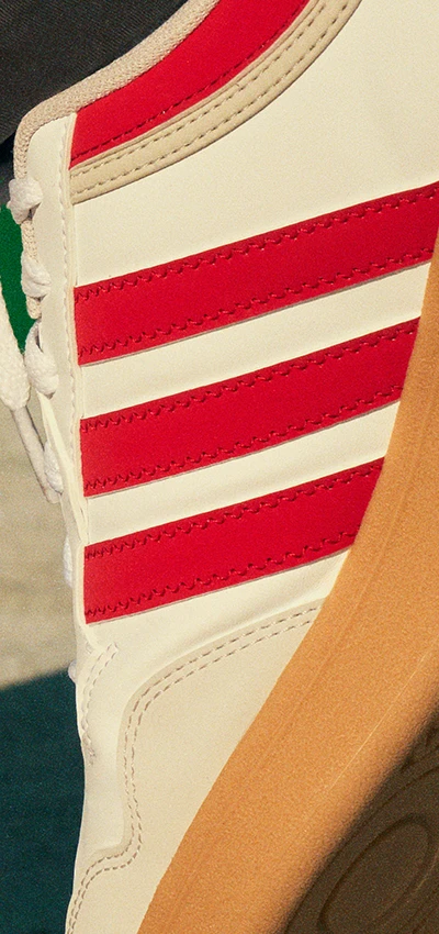 The image shows a person wearing a red and white Adidas sneaker with an orange and gray sole. 