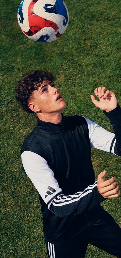 The image shows a person playing soccer on top of what appears to be a patch of grass. The player is looking up at the ball, which seems to be moving towards them, ready to make contact with their head.