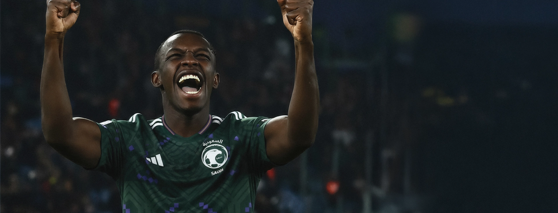 Football player in a green Saudi Arabia adidas jersey celebrating in a stadium. (Photo)