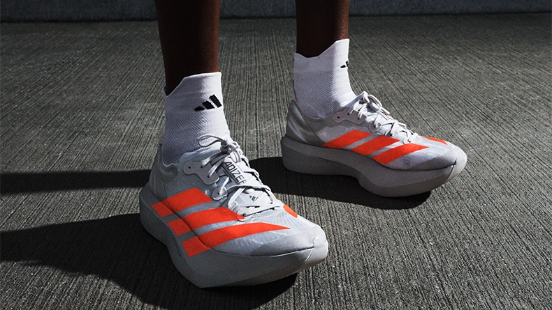 Person wearing white running shoes with red stripes and white socks, standing on asphalt. (Photo)