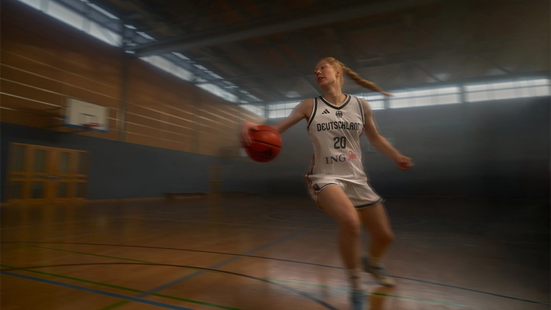 Woman in a white Germany basketball jersey dribbling the ball inside a sports hall. (Photo)