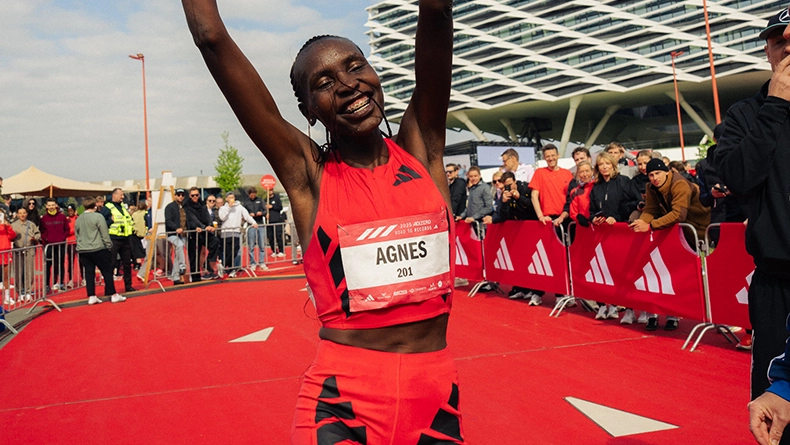 Woman in a red adidas running outfit celebrating with raised arms at a race finish area, spectators standing behind adidas barriers. (Photo)