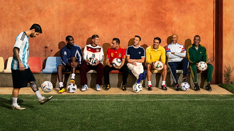 Several men in different adidas football jerseys sitting side by side on a bench, some holding adidas footballs. (Photo)