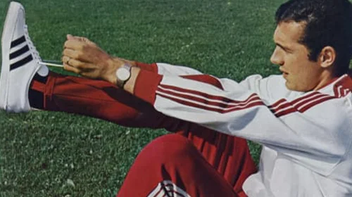 Man stretching on a field wearing an adidas tracksuit. (Photo)