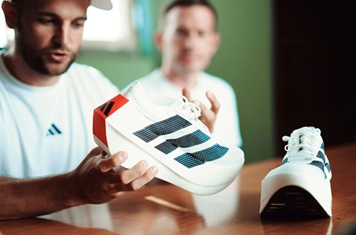 Two men examining and presenting an adidas running shoe at a table. (Photo)
